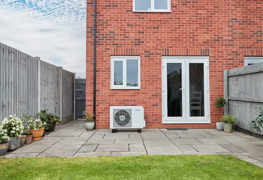 A Bosch air source heat pump installed on the patio of a red-brick home