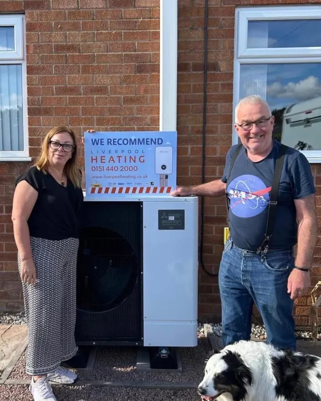 A couple with their new air source heat pump and a Liverpool Heating “We recommend” sign