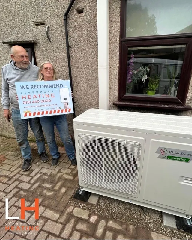 A couple holding a Liverpool Heating “We recommend” sign next to their heat pump