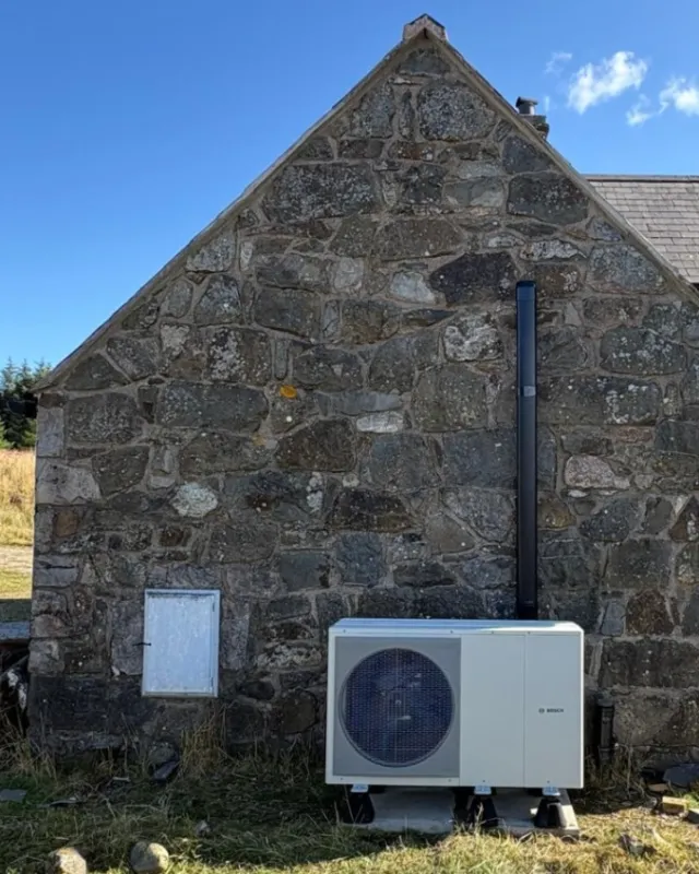 A Bosch air source heat pump fitted against the stone gable of an off-grid rural cottage